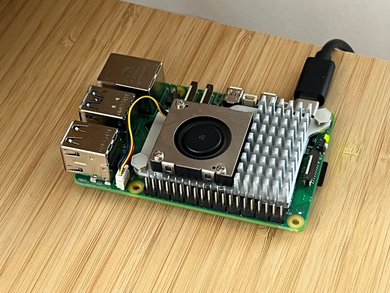 A Raspberry Pi 5 with the official Active Cooler fan and heatsink, on a bamboo desk, with a USB-C power cable plugged in.